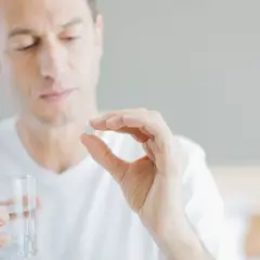 Mann hält Tablette und Glas Wasser, fragt sich, wie viel Magnesium bei Tinnitus hilft.