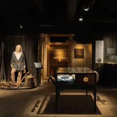 Vikingamuseum Stockholm: en vaxdocka av en viking med yxa, utställningsmontrar med föremål och informationstavlor.