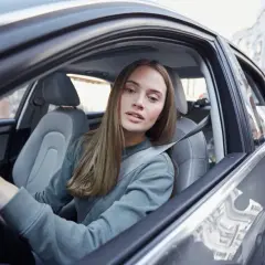 Młoda kobieta, współwłaściciel samochodu poniżej 25 roku życia, prowadzi auto po brukowanej ulicy.