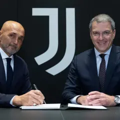 Dwóch mężczyzn w garniturach, prawdopodobnie trenerzy Juventusu, siedzi przy stole. Jeden z nich podpisuje dokumenty.