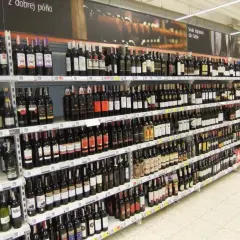 Rzędy butelek wina, w tym wino z suszonych winogron, na półkach sklepowych.