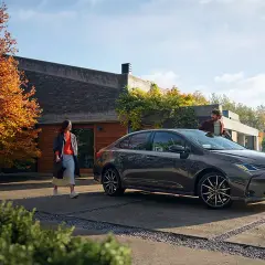 Un hombre y una mujer junto a un Toyota Corolla oscuro frente a una casa moderna.