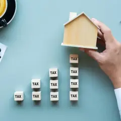 Klocki z napisem "TAX" tworzą rosnący wykres, a dłoń kładzie na szczycie domek. Zastanawiasz się, do kiedy trzeba zapłacić podatek?