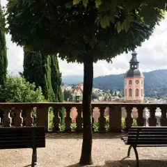 Ein friedlicher Tag in Baden-Baden: Bänke laden zum Verweilen ein, während im Hintergrund ein Kirchturm und grüne Hügel die Aussicht zieren.