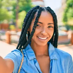Sonrisa radiante de una mujer con distintos tipos de trenzas africanas, luciendo un estilo moderno y seguro.