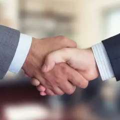 Dwaj mężczyźni w garniturach ściskają sobie dłonie, symbolizując udane joint venture i partnerstwo biznesowe.