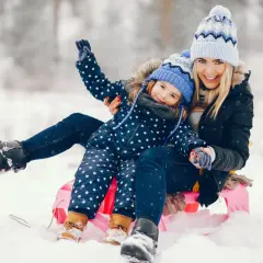 Radosne ferie zimowe 2026 lubelskie! Mama i córka na sankach, śmieją się w śnieżnym krajobrazie.