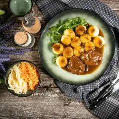 Pyszne niemieckie potrawy: pieczeń wołowa w sosie z kluskami ziemniaczanymi i surówką z kapusty i marchewki.