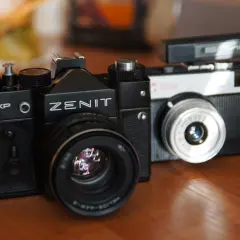 Dwa klasyczne aparaty na film: czarny Zenit 12XP i srebrno-czarny Smiena z lampą błyskową.