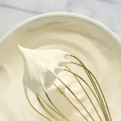 Batidor con nata montada cremosa en un bol blanco. El proceso de montar nata está casi completo.