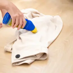 Jak wyczyścić żywicę z ubrania? Ktoś aplikuje płyn z niebieskiej butelki na jasny materiał.