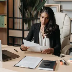 Kobieta w biurze analizuje dokumenty, zastanawiając się, ile trwa staż z urzędu pracy. Na biurku laptop, telefon i notatnik.