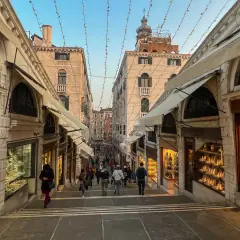 Schody na moście Rialto w Wenecji, z witrynami sklepów z biżuterią po bokach. Tłum ludzi schodzi w dół.