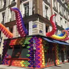 Tentacules colorés géants sortent d'un bâtiment orné de motifs arc-en-ciel, un décor festif pour ce bar gay à Paris.
