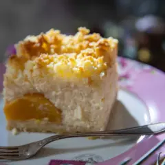 Pyszny sernik z brzoskwiniami, posypany kruszonką, na różowym talerzyku. Idealny na deser.