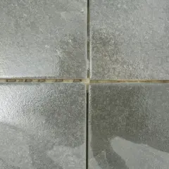 Dettaglio di quattro piastrelle grigie con fughe vuote, pronte per essere riempite. Una guida visiva su come riempire le fughe delle piastrelle.