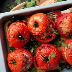 Six tomates farcies dorées, garnies d'une farce savoureuse et parsemées de persil frais, dans un plat de cuisson.