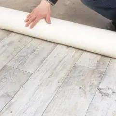 Eine Rolle Unterlage liegt auf einem Holzboden. Sie ist ideal, wenn Sie sich fragen, was kommt unter PVC Boden.