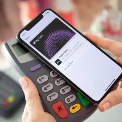 Dłoń trzyma iPhone'a nad terminalem płatniczym, ekran pokazuje "Apple Cash". To pokazuje, jak aktywować kartę i zacząć płacić.