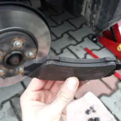 Wymiana klocków hamulcowych w Oplu Insignia z elektrycznym hamulcem postojowym. W dłoni trzymam zużyty klocek.