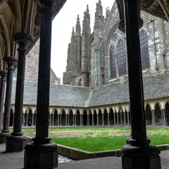 Ein Blick durch die Säulenhalle auf den Kreuzgang des Mont Saint Michel innen. Grüne Wiese und gotische Architektur.