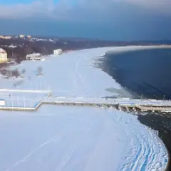 Zimowy spacer po molo, gdzie zimą nad morze przyciąga biel śniegu i lodowe krajobrazy. Widok na zamarznięte plaże i budynki w oddali.