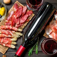 Un bicchiere di vino rosso, una bottiglia, salumi, olive e grissini avvolti nel prosciutto, un'ambientazione perfetta per la vinificazione in rosso.