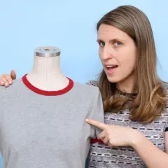 Woman points to a grey t-shirt on a mannequin, demonstrating how to sew a shirt.