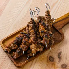 Cinq brochettes d'agneau grillées, savoureuses et légèrement caramélisées, reposent sur un plateau en bois.