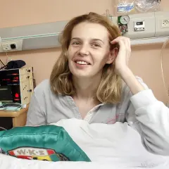Uśmiechnięta córka Agaty Mróz w szpitalnym łóżku, otoczona sprzętem medycznym.