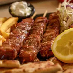 Pyszne souvlaki na patyczkach, podane z frytkami, pitą, surówką i cytryną.
