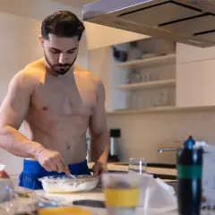 Muskulöser Mann bereitet in der Küche eine Mahlzeit zu. Kohlenhydrate sind wichtig für den Muskelaufbau.