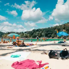 Gente disfrutando de unas **vacaciones agosto 2026** en una playa tropical, con aguas turquesas y vegetación exuberante.