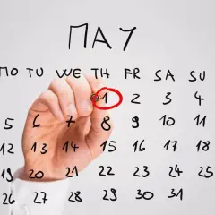 Ręka zaznacza czerwonym markerem 1 maja na kalendarzu. Planujesz dpd przekierowanie paczki?