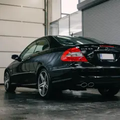 Czarny Mercedes CLK 63 AMG z podwójnymi końcówkami wydechu, zaparkowany w garażu z podnoszoną bramą.
