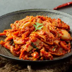 Miseczka z pikantnym kimchi, ozdobiona listkiem kolendry.