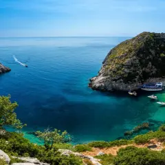 Malownicza zatoka z krystalicznie czystą wodą i plażą, gdzie cumują łodzie. Idealne miejsce na wakacje, zastanawiasz się, ile się leci do Albanii?