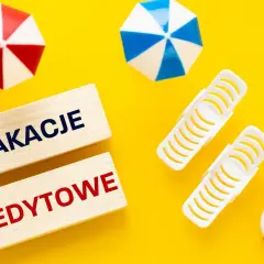 Drewniane klocki z napisem "WAKACJE KREDYTOWE" na tle letnich akcesoriów. Planujesz wakacje kredytowe 2026?