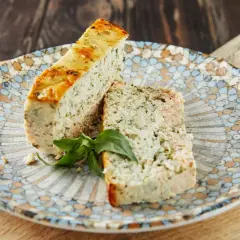 Deux tranches de terrine de poisson aux herbes, garnies d'une feuille de basilic, sur une assiette décorée.