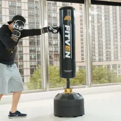 Man in boxing gloves practices how to punch a punching bag in a bright room with a city view.