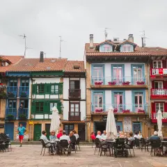 Fachada de casas coloridas en Hondarribi, con balcones floridos y gente disfrutando en terrazas.