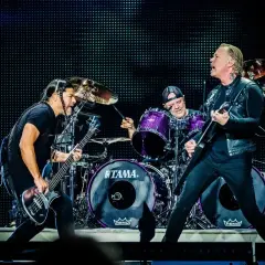 Duński zespół rockowy na scenie: basista z warkoczami, perkusista w fioletowym zestawie i gitarzysta w skórzanej kurtce.