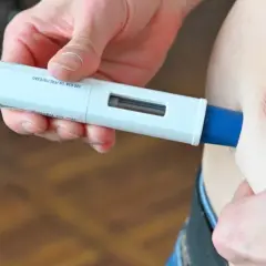 Eine Hand hält einen Aimovig-Injektor, bereit zur Anwendung.