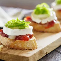 Deliciosos pinchos y tapas originales: rebanadas de pan con queso de cabra, mermelada de pimientos y cebolla morada.