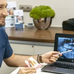Dentysta omawia z pacjentką prawidłowe czyszczenie dziąseł, pokazując model zębów i zdjęcie rentgenowskie.