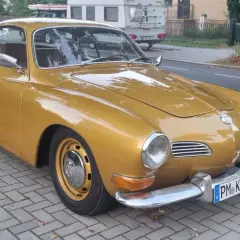 Złoty Volkswagen Karmann Ghia zaparkowany na chodniku z kostki brukowej.