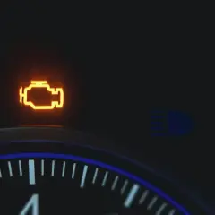 Pomarańczowa kontrolka **check engine** świeci na desce rozdzielczej. Obok widać ikonę świateł drogowych.