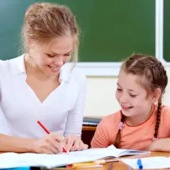 Nauczycielka pomaga uczennicy w lekcjach przy biurku.