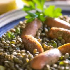 Un plat de lentilles saucisses, garni de persil frais, servi dans une assiette bleue et blanche.