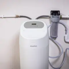 Instalación de descalcificador Equation con filtro de agua. Sistema de tuberías blancas y mangueras grises conectadas a la unidad.